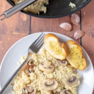 Birds eye view of a plate of this delicious 30-minute mushroom risotto served with 2 slices of garlic bread and the other half of the cooked risotto still in the pan.