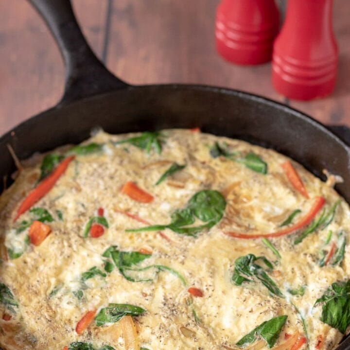 Red pepper and spinach frittata cooked in a skillet and ready to serve. Salt and pepper cellars in the background.