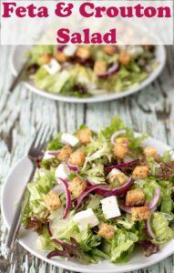 Two served plates of feta and crouton salad one in front of another ready to eat with a fork on the side. Pin title text overlay at top.