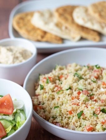 Display of main bowl of tabbouleh couscous with side salad, hummus and at the back a plate of flat breads.