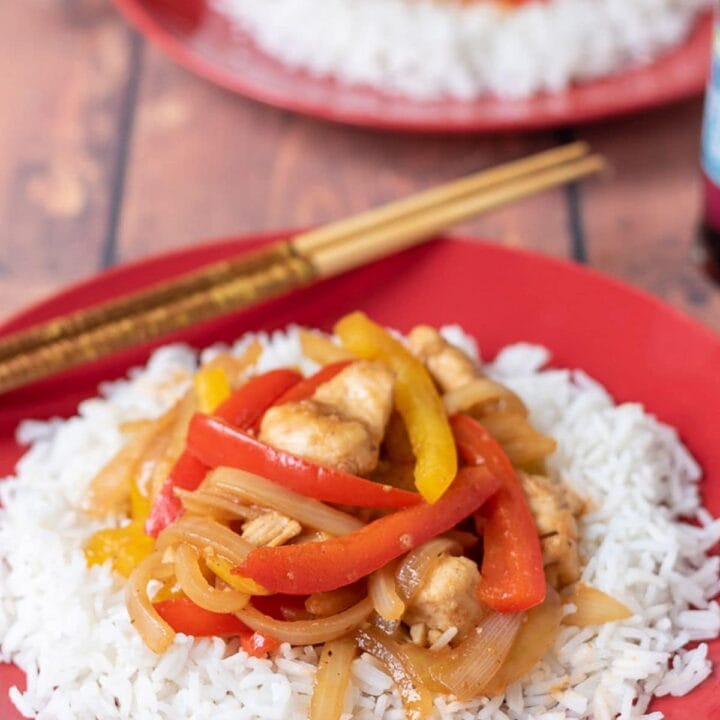 Two plates of easy sweet and sour chicken served on basmati rice one in front of the other with chopsticks on.