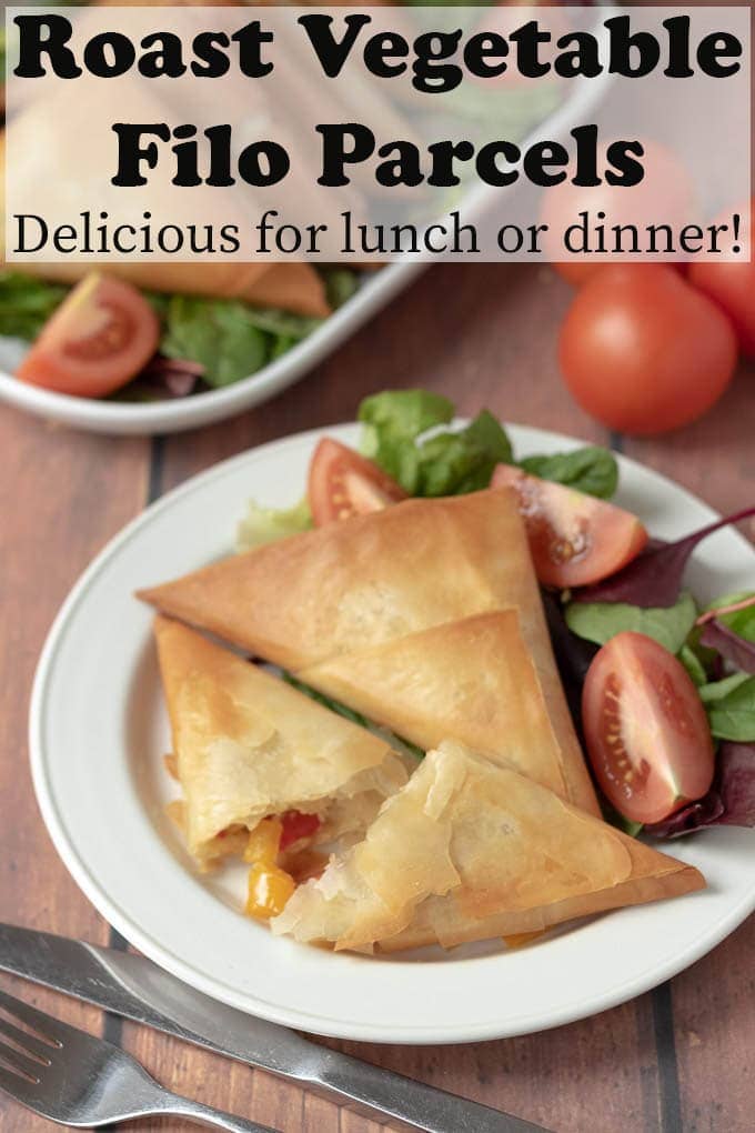Three roast vegetable filo parcels on a plate. One cut so the roast vegetable filling is falling out. A light salad of lettuce and tomatoes served on the plate too.