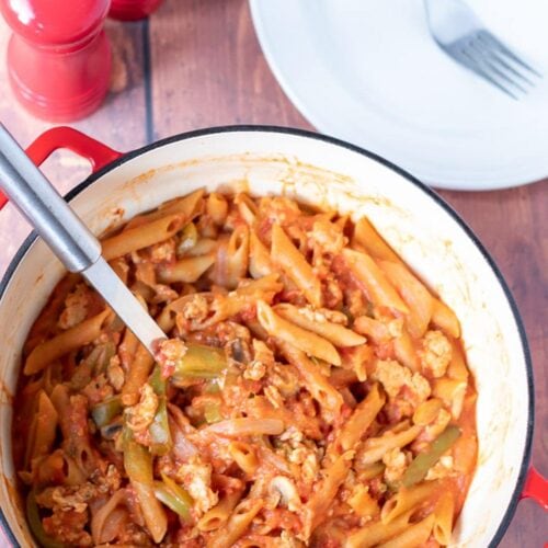 Birds eye view of one pot sausage pasta with a serving spoon in it. Ready to serve with salt and pepper and a serving plate at the top.