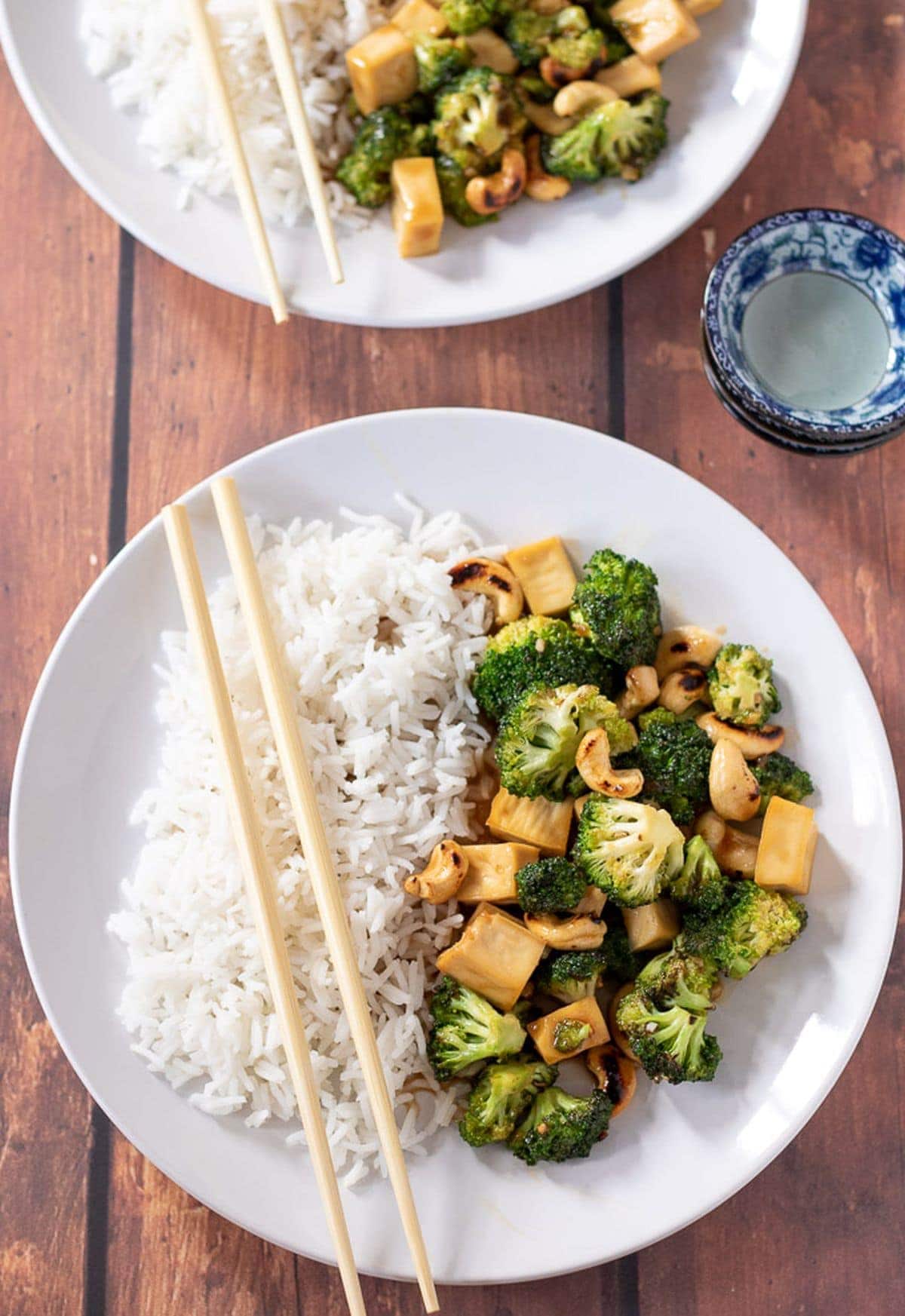 Birds eye view of two plates of sticky peanut butter tofu stir-fry served with rice and chop sticks placed over plates.
