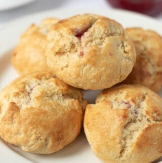 A plate of raspberry buns with a jar of raspberry jam in the background.