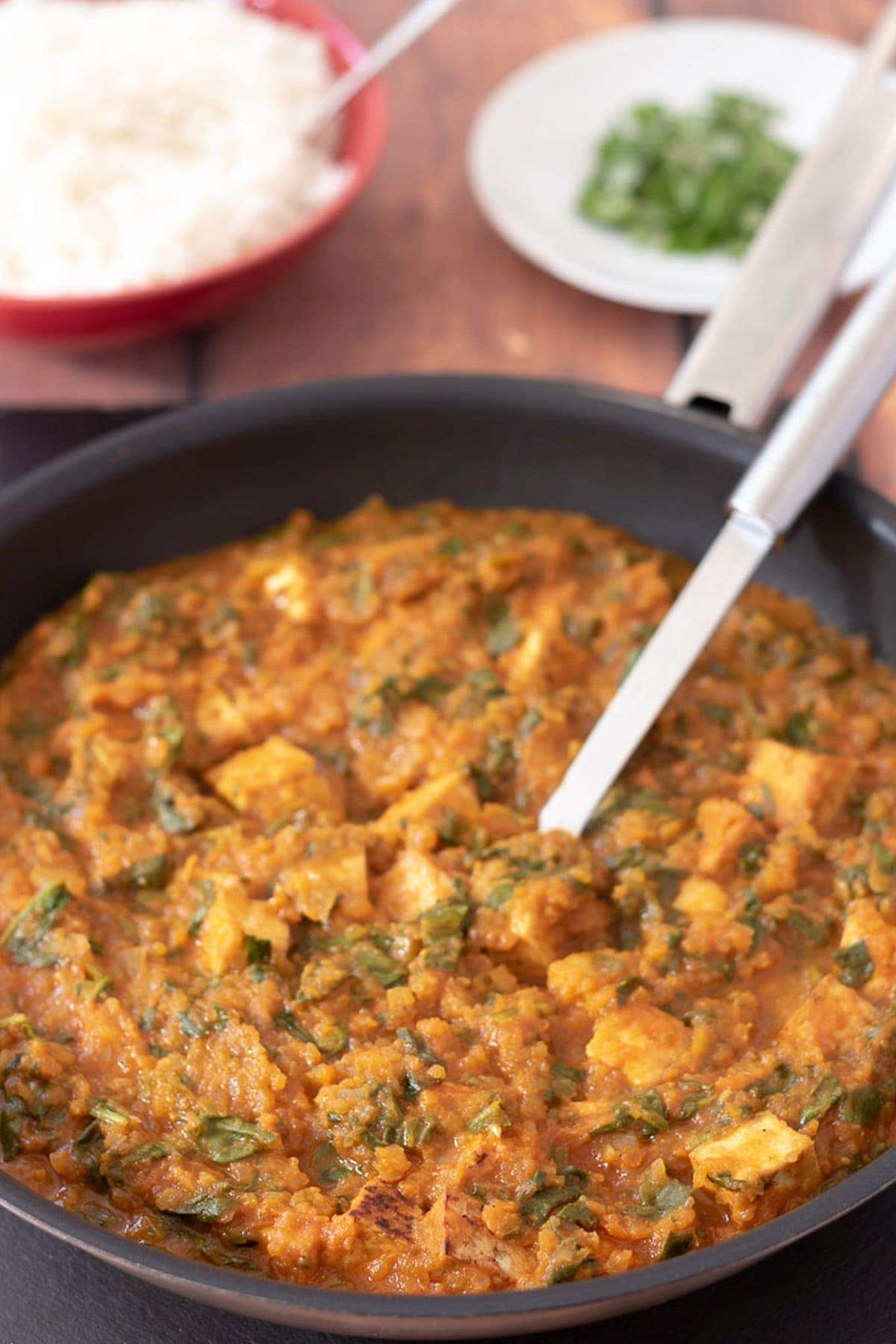 A pan of cooked tofu spinach curry with a spoon in it ready to serve.