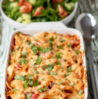 Chicken and chorizo pasta bake with a serving spoon to the right and a bowl of side salad in the background.