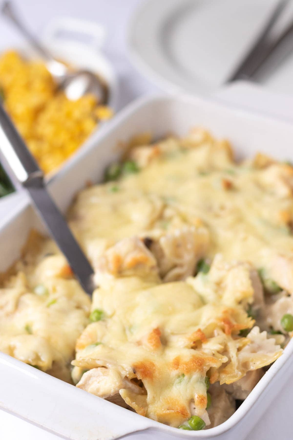 A serving spoon lifting out a portion of honey mustard chicken pasta bake from the casserole dish.