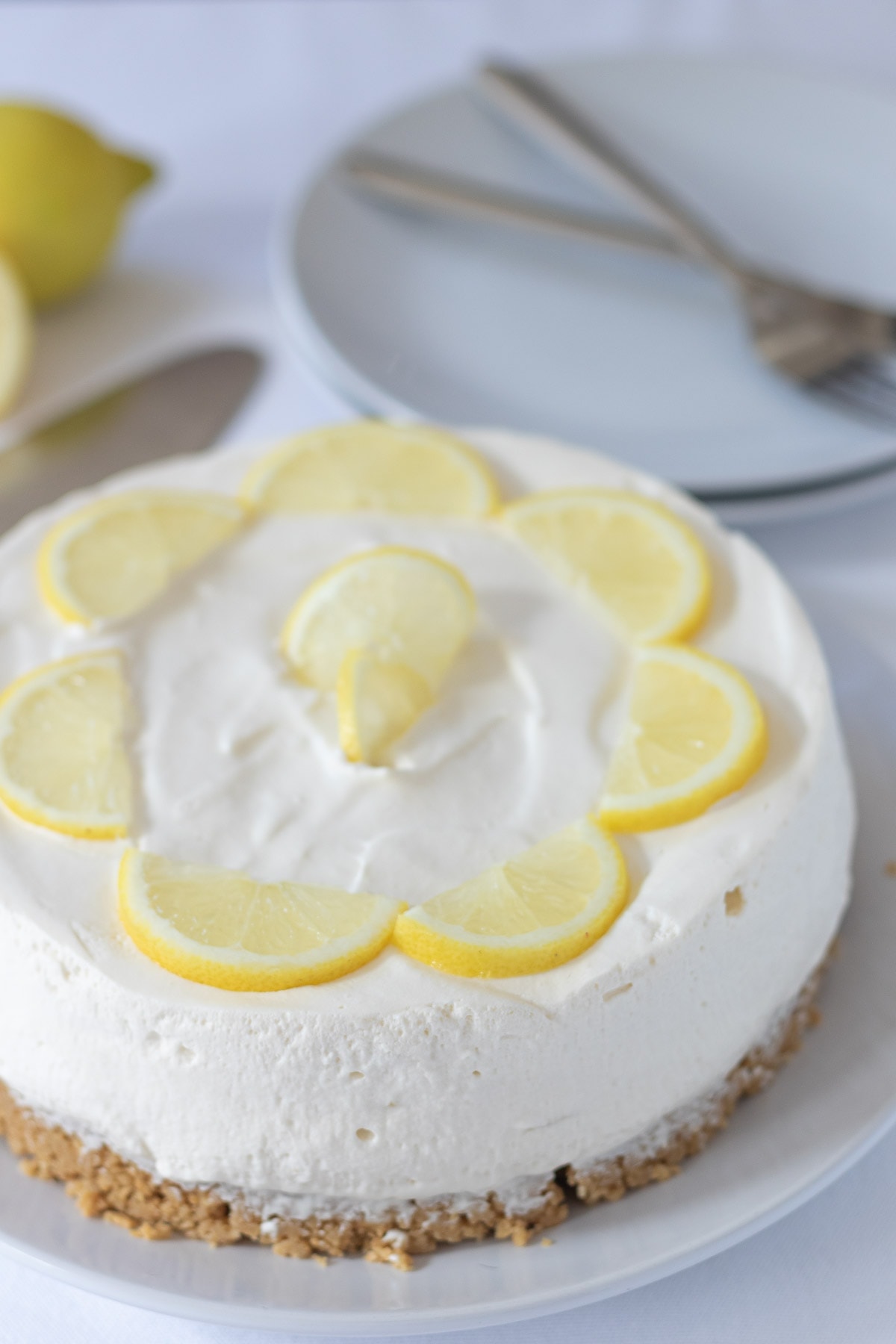 Daily free cheesecake decorated with slices of lemon with serving plates and forks on in the background.