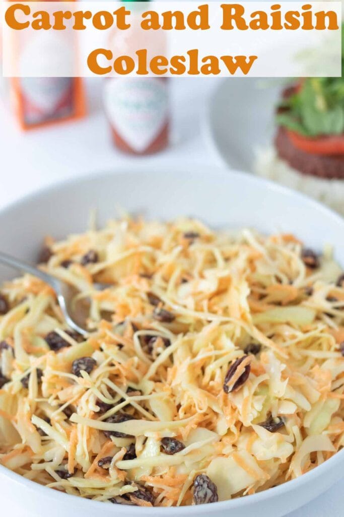 A large salad dish of carrot and raisin coleslaw with a serving spoon in. Pin title text overlay at top.