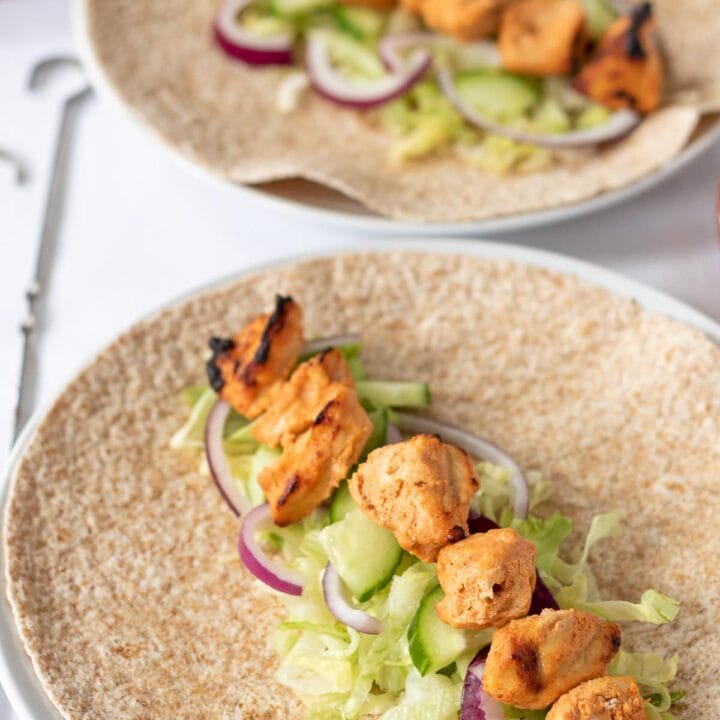 Two chicken tikka wraps assembled on plates and ready to be rolled.
