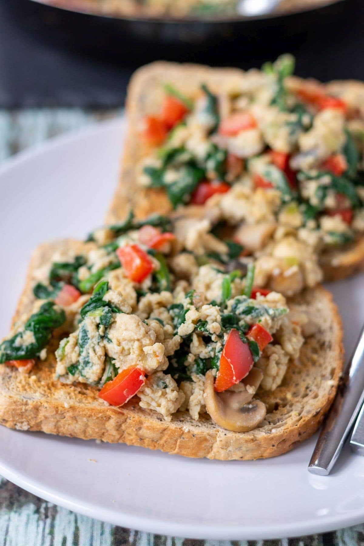 Two slices of toast with vegetable scrambled eggs on top.