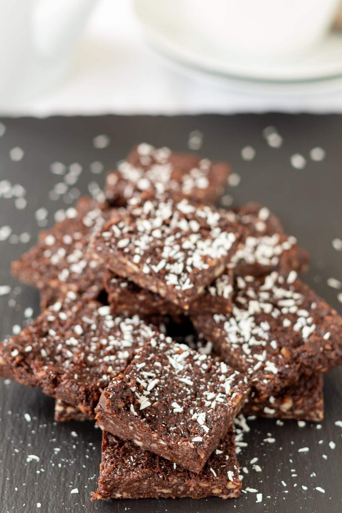 Close up view of a stack of no bake chocolate brownies on a slate decorated with grated coconut.