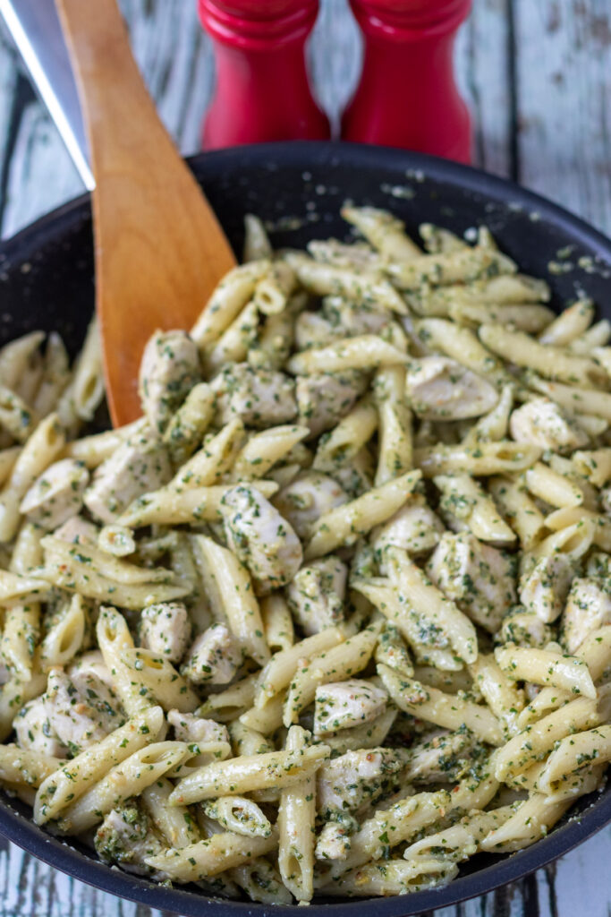 Pasta, pesto and chicken all mixed together in a large pan.