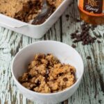 A bowls of chocolate peanut butter baked oats with a spoon in front. Rest of the recipe ins a casserole dish in the background with a jar of honey beside.