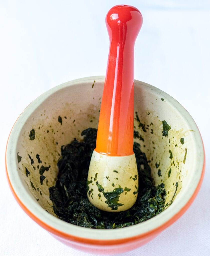 Basil leaves bashed into a pulp in a pestle and mortar.