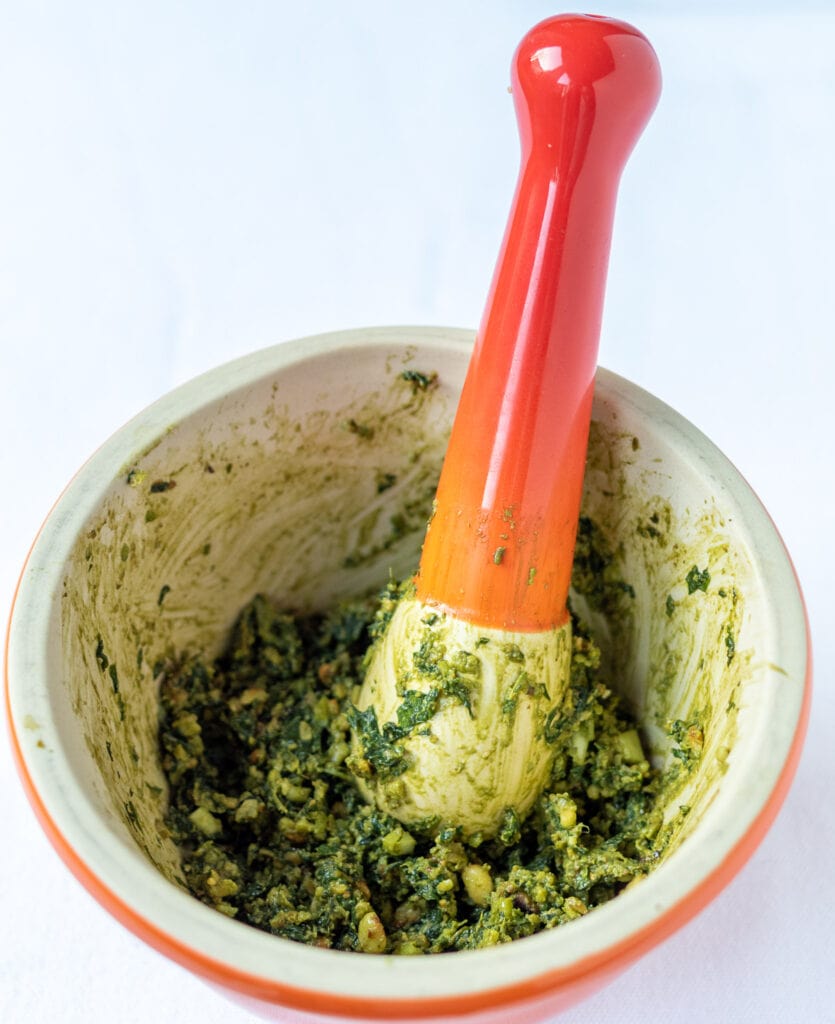 Pine nuts and garlic added to bashed pulped basil leaves in a pestle and mortar.