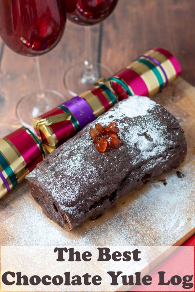 Best chocolate yule log on a board decorated with icing sugar and christmas decorations around. Pin title text overlay at bottom.