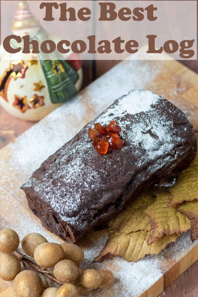 Home made chocolate log on a board topped with red berries and icing sugar. Christmas decorations around.