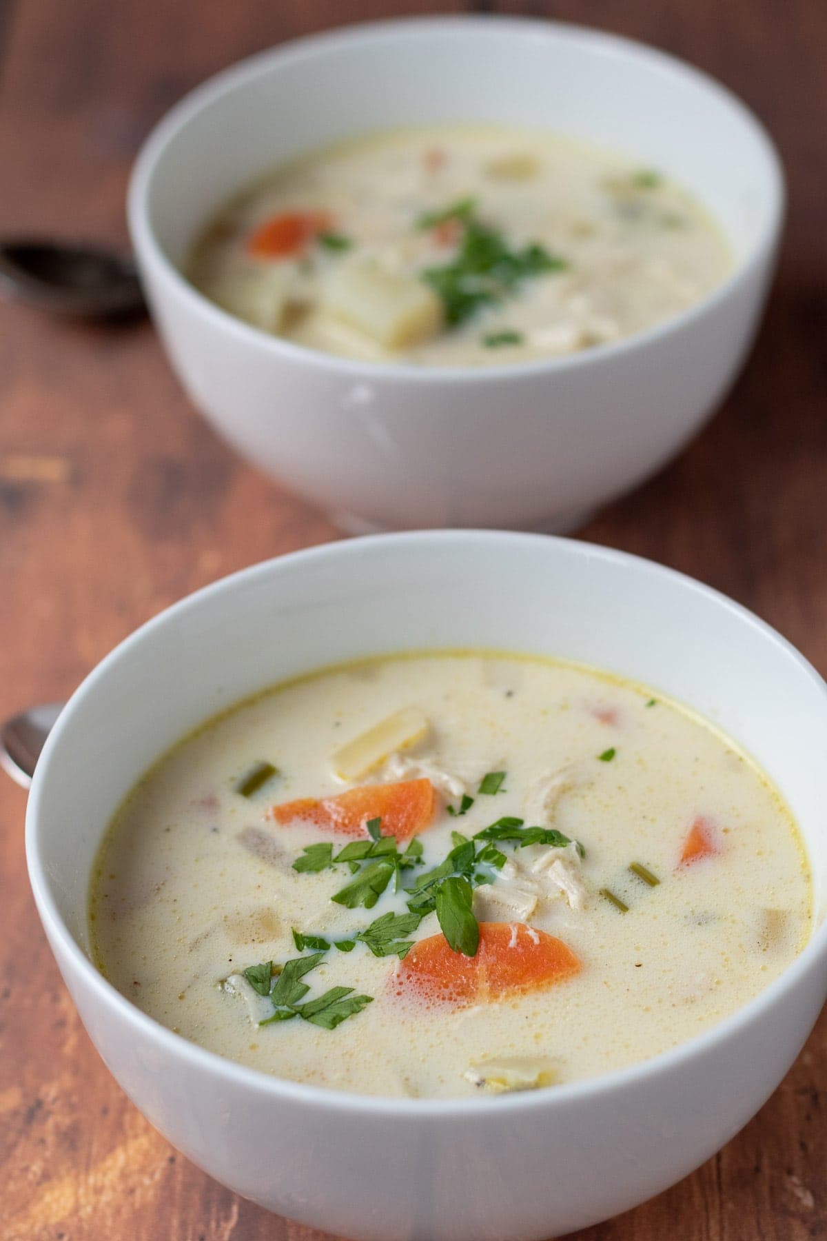 Two bowls of creamy chicken potato soup one in front of the other.