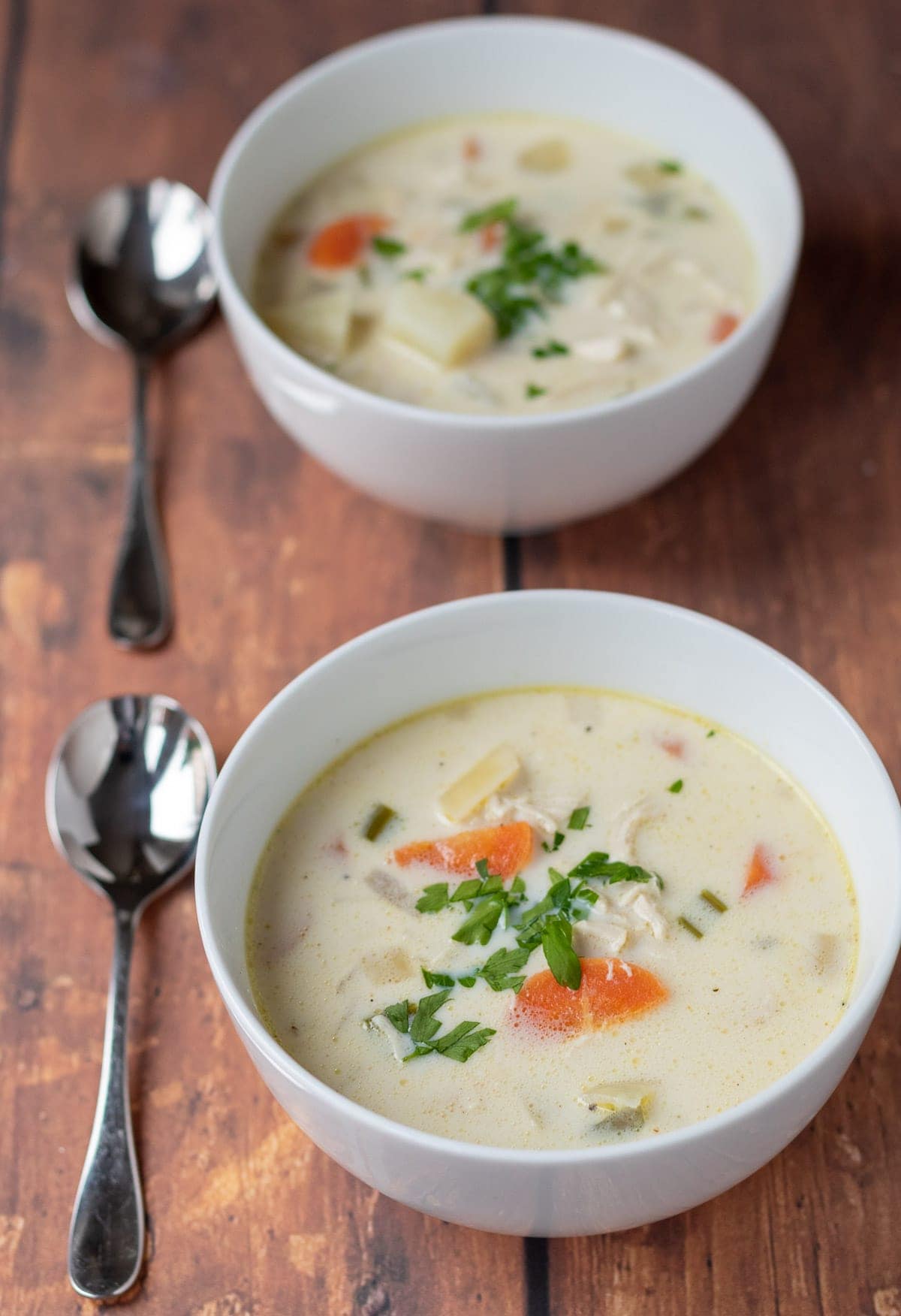 Two bowls of healthy creamy chicken potato soup with spoons beside.