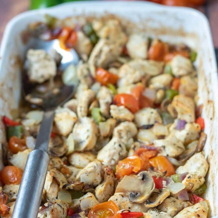 Baked chicken and mixed vegetables cooked in a stoneware serving dish with a serving spoon to the left hand side.