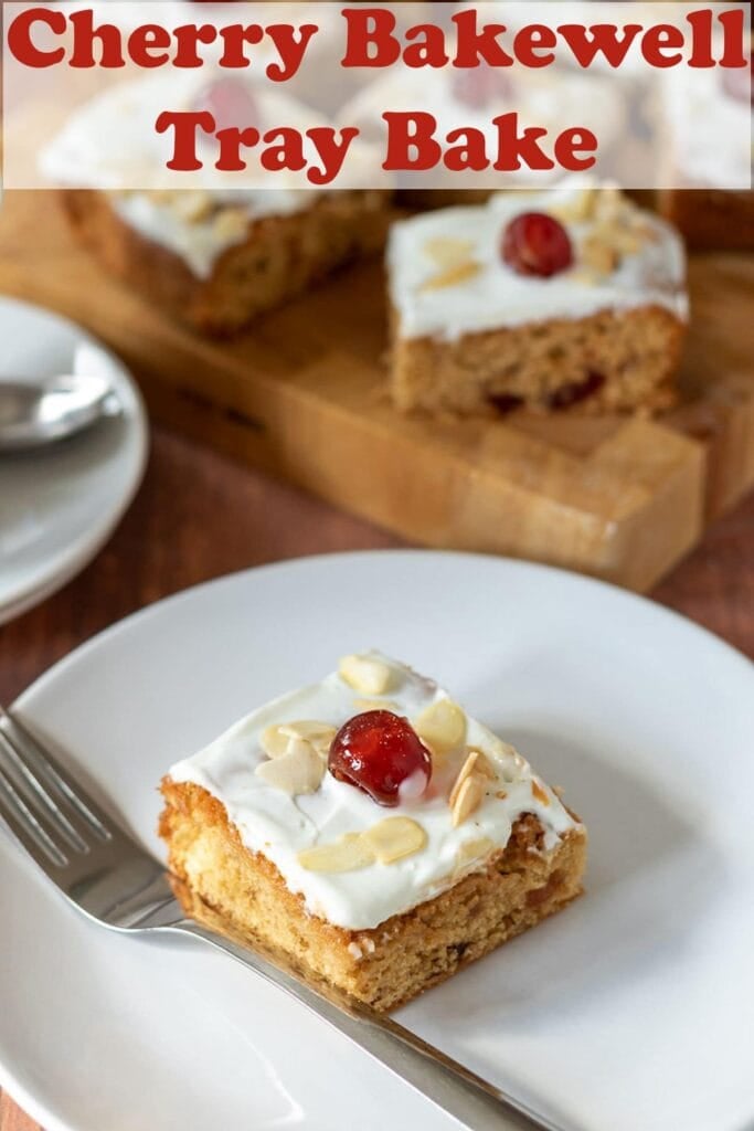 A slice of cherry bakewell tray bake topped with cream cheese icing and a glace cherry on a plate. Rest of the slices on a board in the background. Pin title text overlay at top.