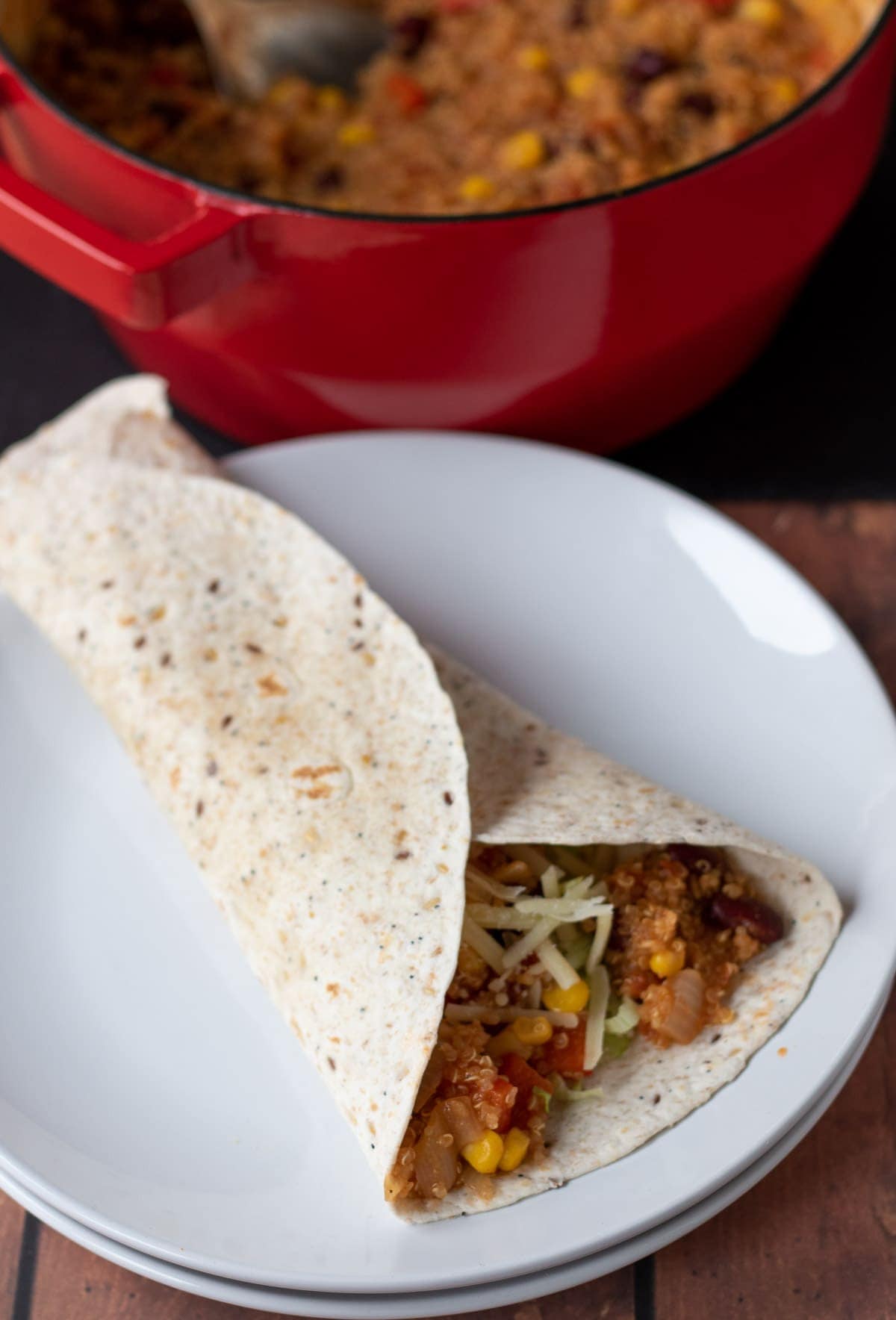 A closed wrap filled with quinoa chilli on two white plates. Casserole pot at the top.