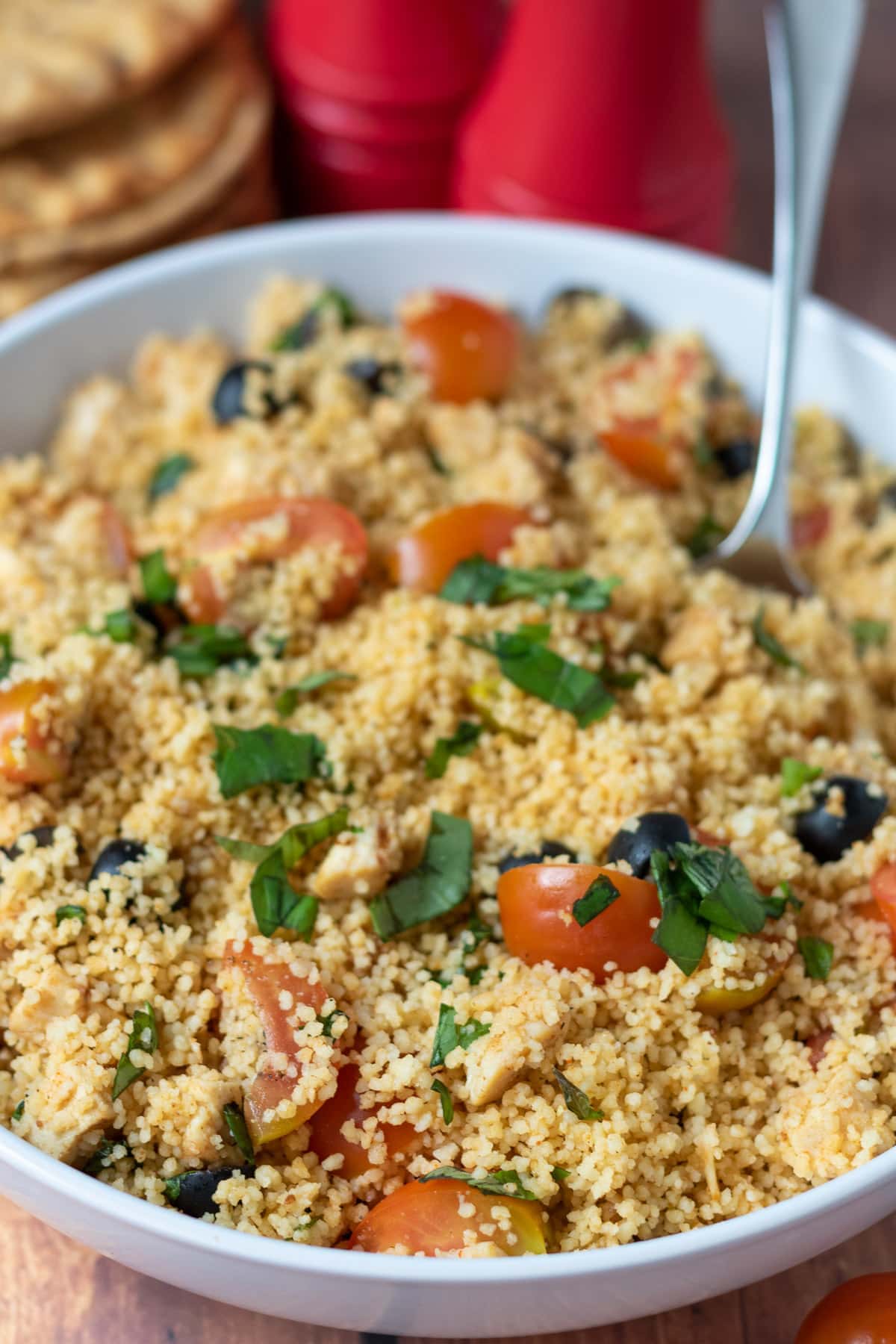 A bowl of fluffy chicken and couscous salad with a serving spoon in.