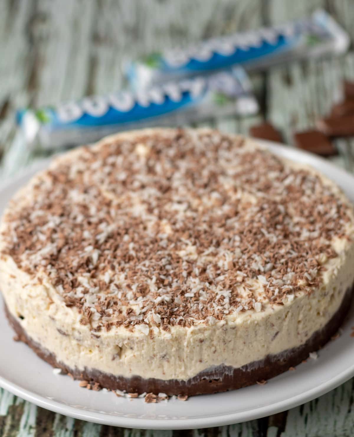 No-bake Bounty coconut cheesecake uncut sitting on a plate with unwrapped bounty bars in the background.