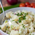 A bowl of healthy potato salad garnished with chives and with a serving spoon in.