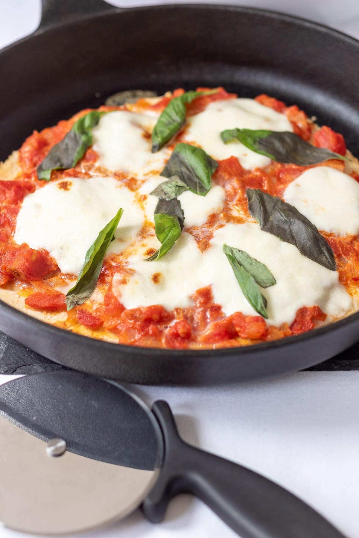 A skillet with a Neapolitan pizza in it and a pizza cutter in front.