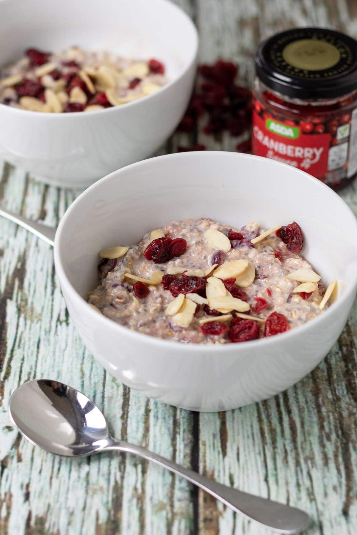 Two bowls of cranberry oats breakfast with spoon in front. A jar of cranberry sauce at the back right.