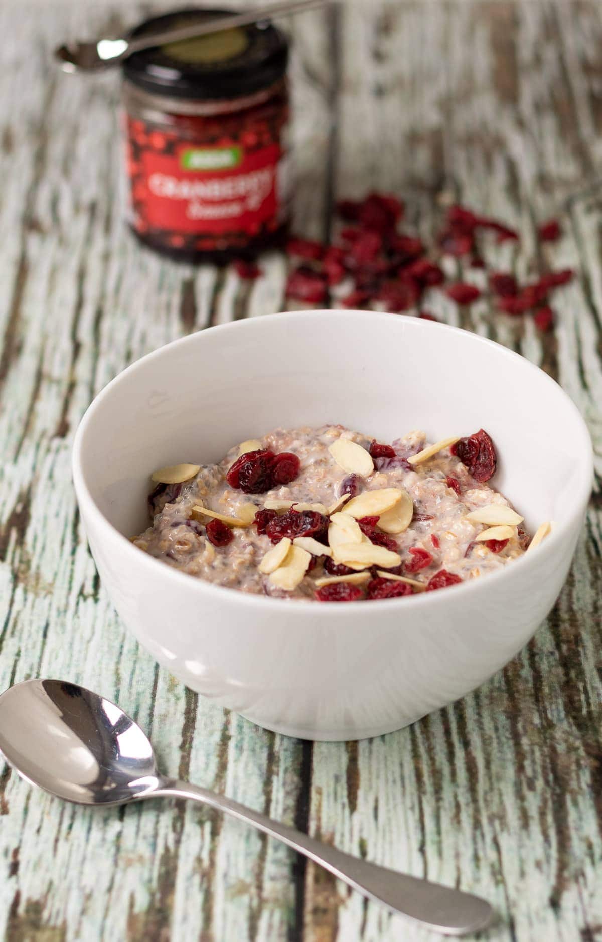A bowl of cranberry overnight oats with spoon in front and jar of cranberry sauce in the background.