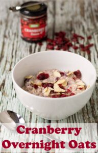 A bowl of cranberry overnight oats with a jar of cranberry sauce and cranberries sprinkled around at top. Pin title text overlay at bottom.