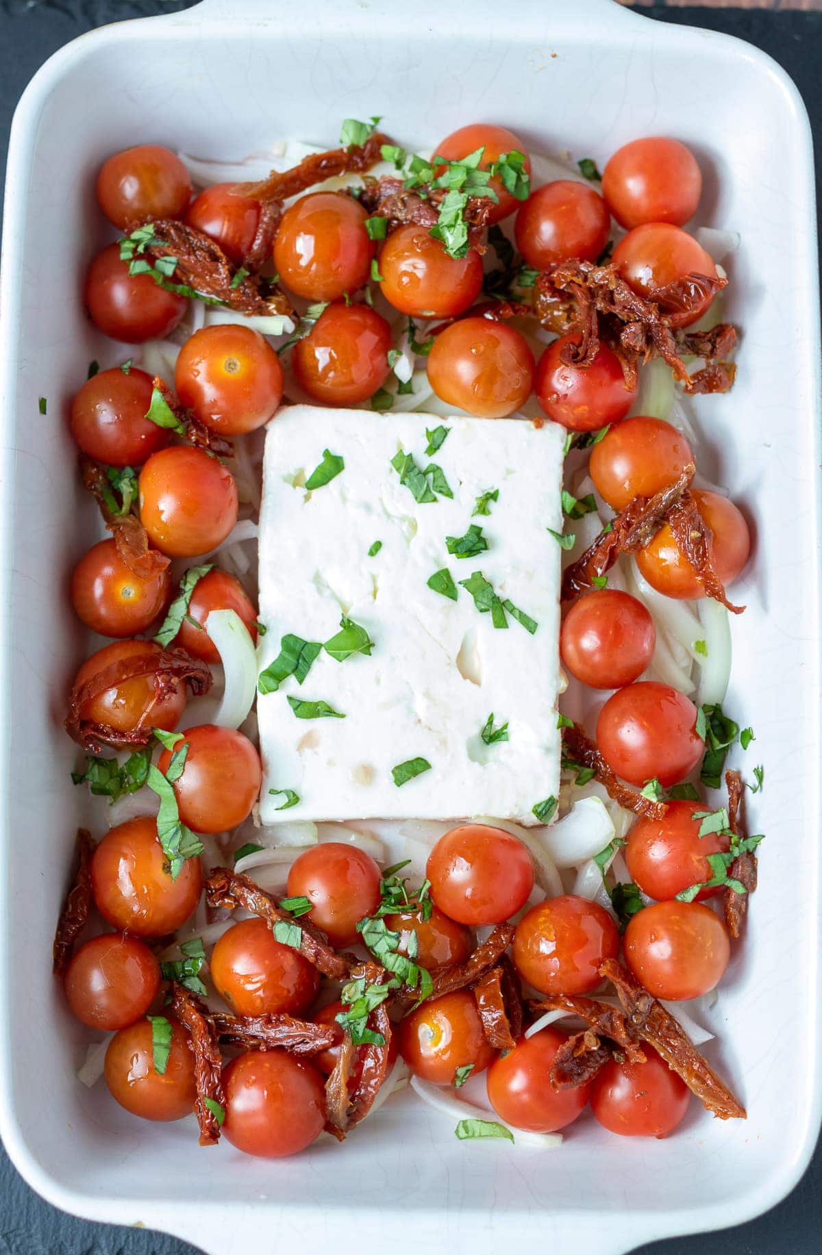 Step 1 of image showing how to make healthy baked feta pasta. A stoneware dish with a block of feta cheeese in and cherry tomatoes around.