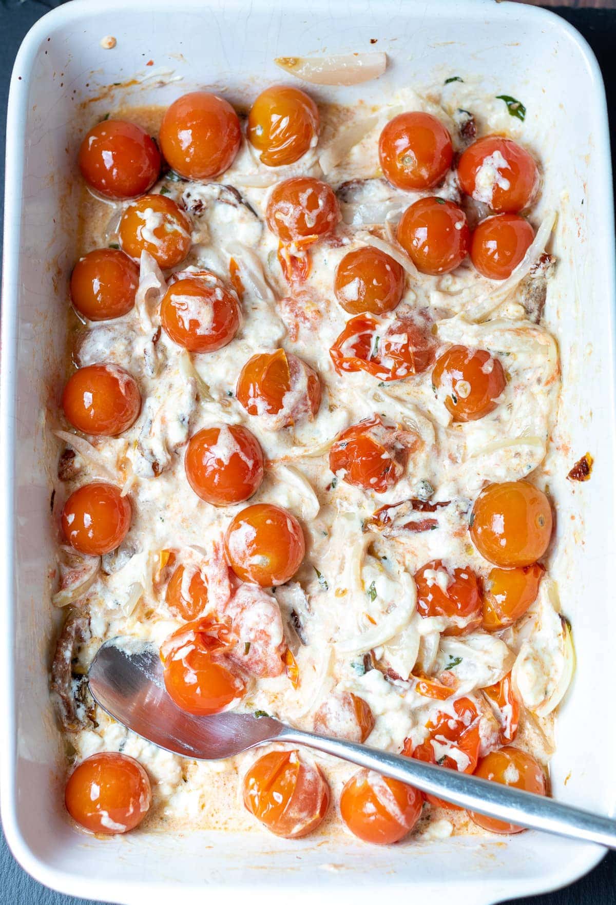Step 3 of images showing how to make healthy baked feta pasta. A stoneware dish showing baked feta cheeese mixed together with the tomatoes.