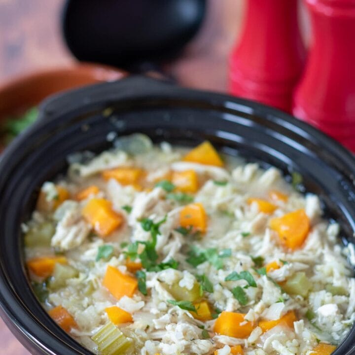 Slow cooker chicken and rice soup in a slow cooker. Salt and pepper cellars and soup ladle in the background.