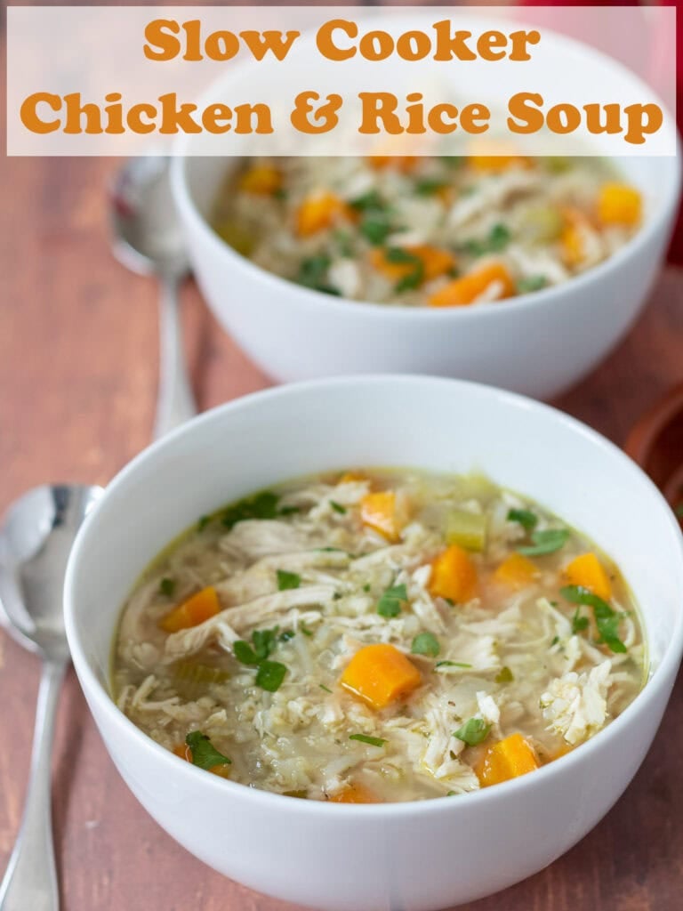 Two bowls of chicken and rice soup which were made in a slow cooker one in front of the other. Soup spoons to the left. Pin title text overlay at top.