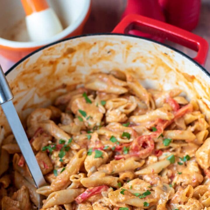 One pot cajun chicken pasta in a large casserole pot with a serving spoon in. Pestle and mortar and salt and pepper cellars in the background.