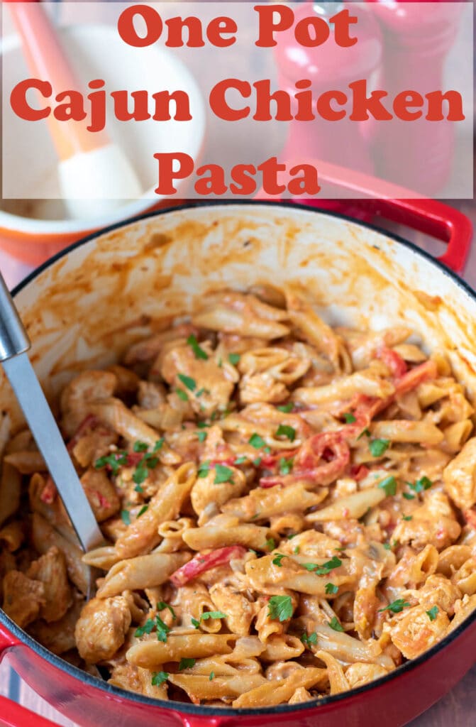 One pot Cajun chicken pasta cooked in a red casserole pot with a serving spoon in. Pin title text overlay at top.