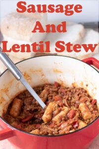 Sausage and lentil stew in a casserole pot with a serving spoon in. Pin title text overlay at top.