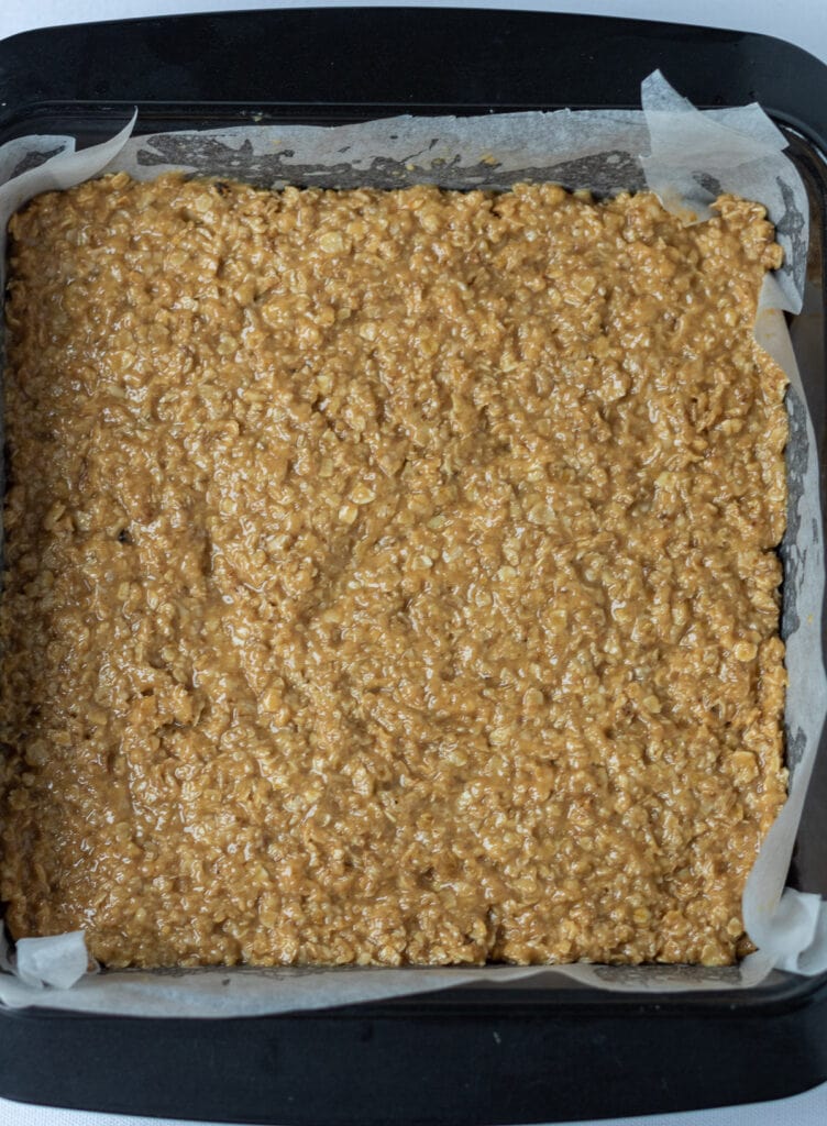 Oats coated mixture pressed into square baking tin.