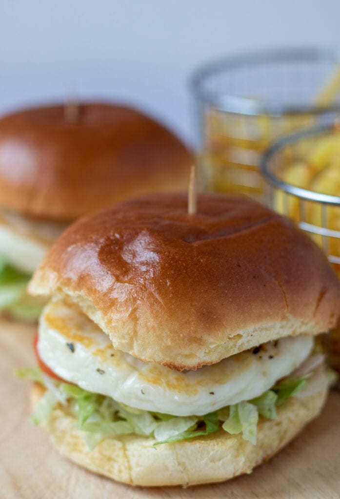 Close up of spicy red pesto halloumi burgers with baskets of chips in the background.