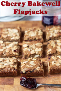 Nine cherry bakewell flapjack squares on a chopping board. Pin title text overlay at top.