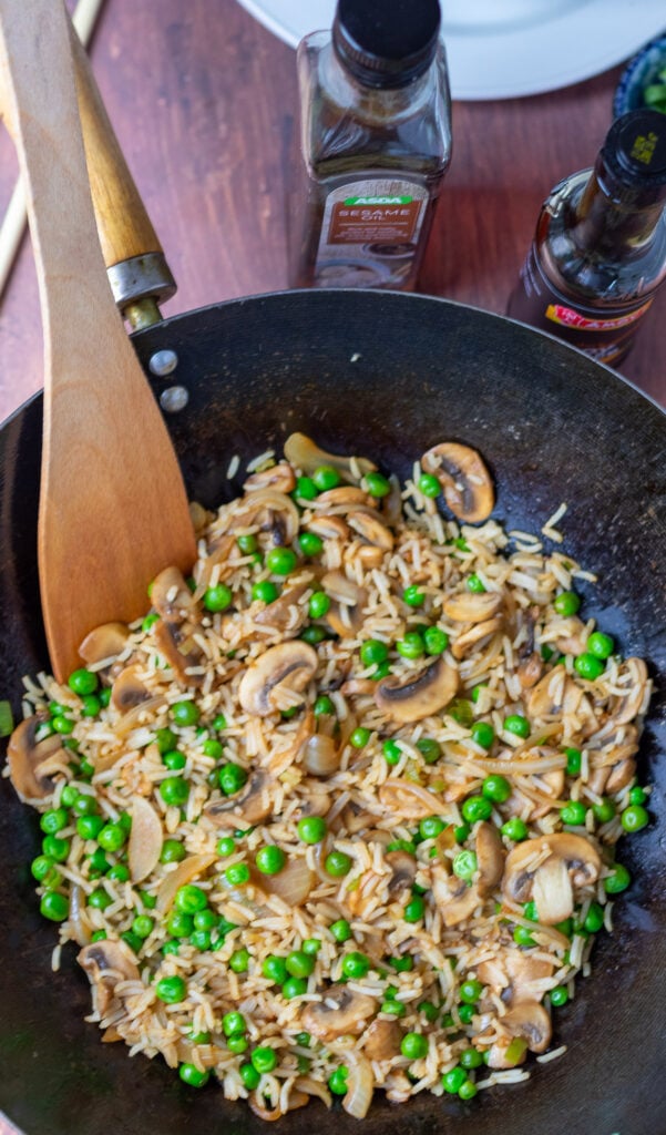 Birds eye view of a wok with leftover mushroom and rice stir-fry being stirred with a wooden spatula.