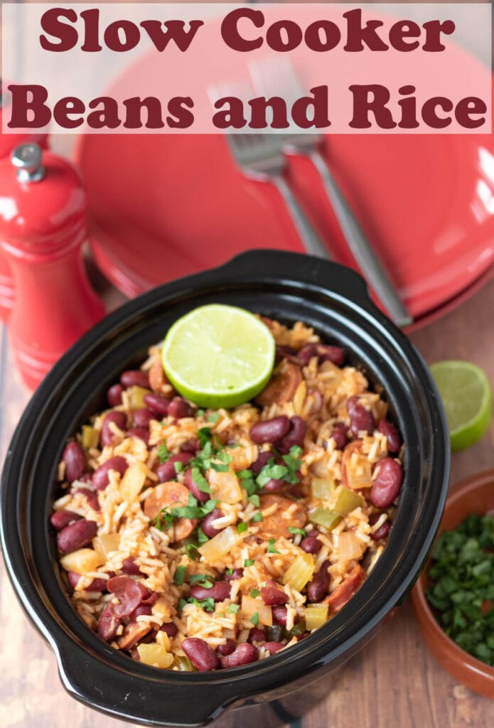Slow cooker beans and rice in a slow cooker with half a lime on top. Plates with forks on in the background. Pin title text overlay at top.