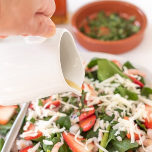 A plate of baby spinach salad and prawns with dressing being poured over.
