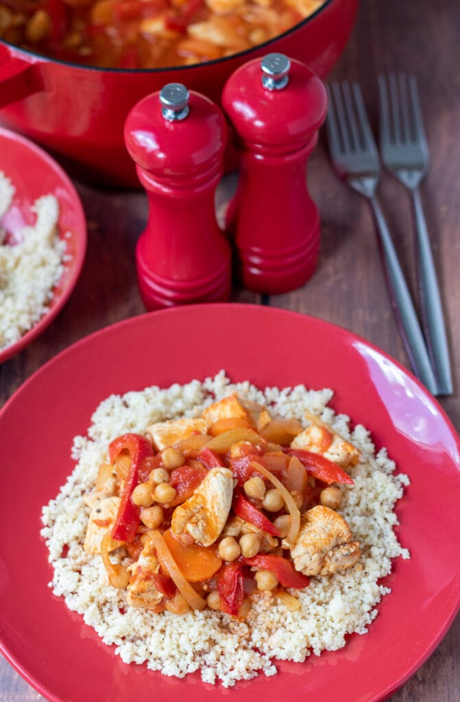 Chicken and chickpea stew served on a bed of couscous. Salt and pepper cellars, two forks, dish of couscous and edge of casserole dish above.
