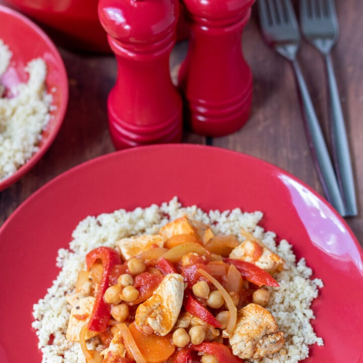 Chicken and chickpea stew served on a bed of couscous. Salt and pepper cellars, two forks, dish of couscous and edge of casserole dish above.